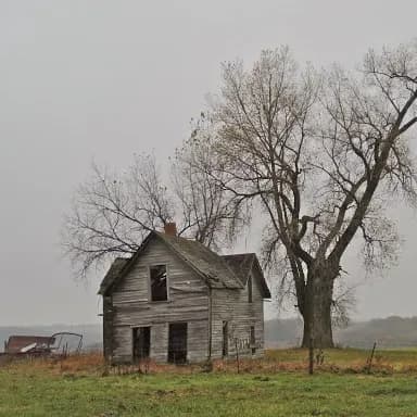A white house that's falling in on itself and decaying on an abandoned farm.