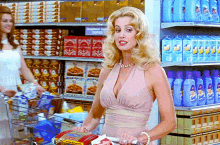 A blonde woman walking down a supermarket with her cart full.